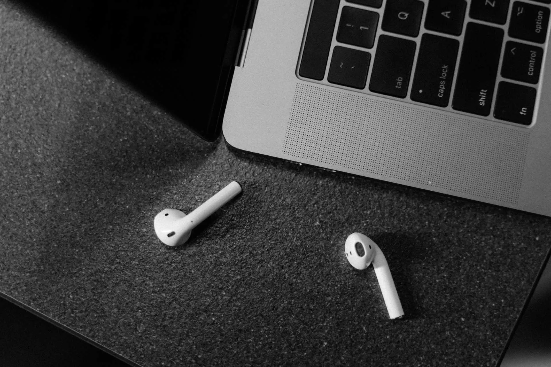 A pair of Apple Airpods next to a Macbook.